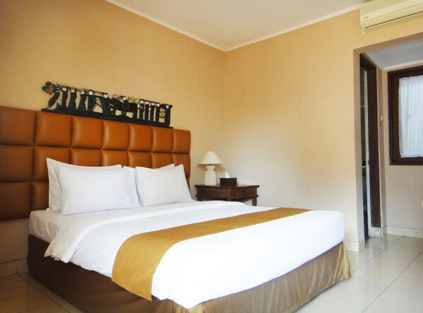 A neatly made bed with white linens and a brown accent, a wooden nightstand with a lamp, and a headboard with a decorative piece.