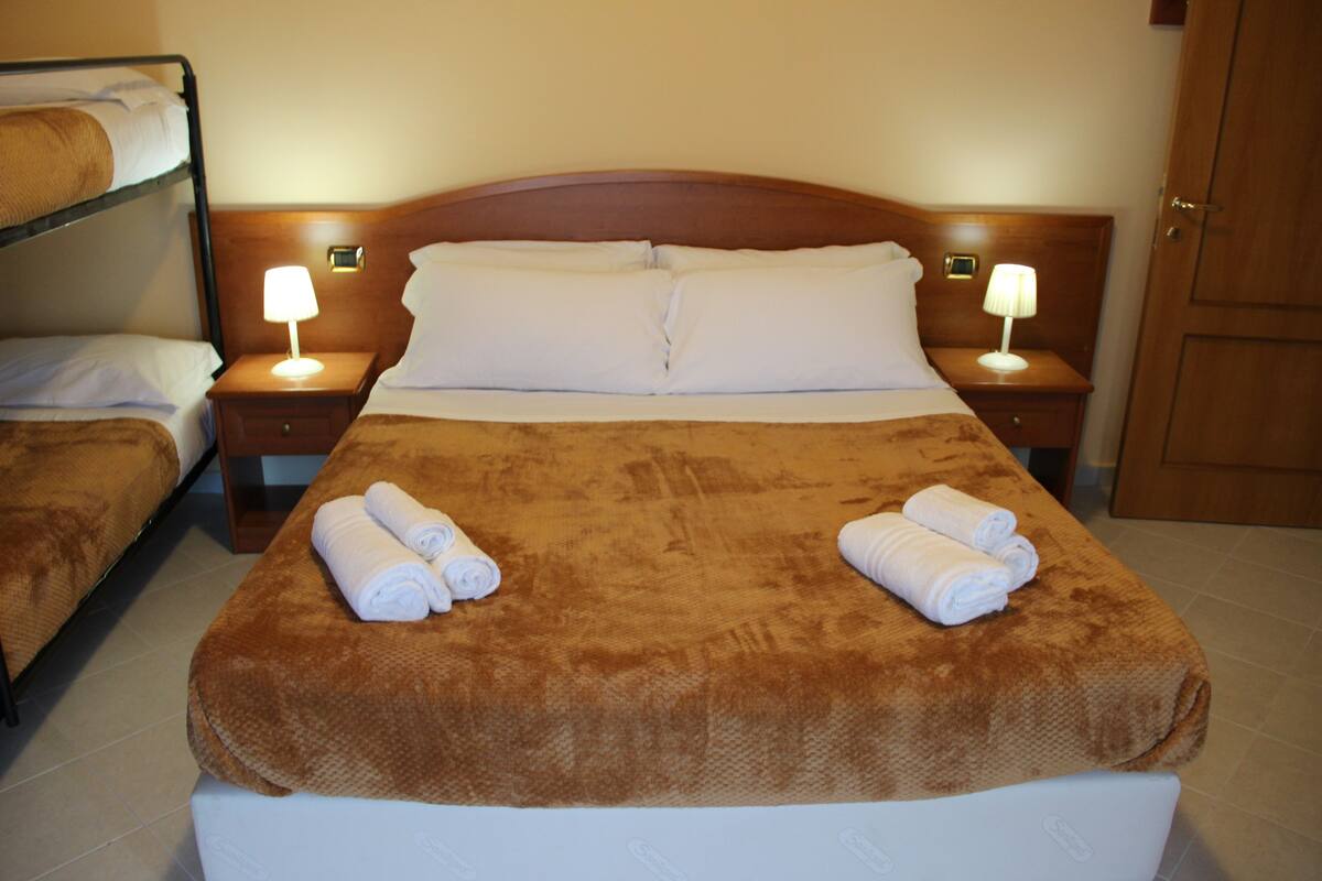 Habitación de hotel con una cama grande, dos mesitas de noche con lámparas, un cabecero de madera y una puerta.
