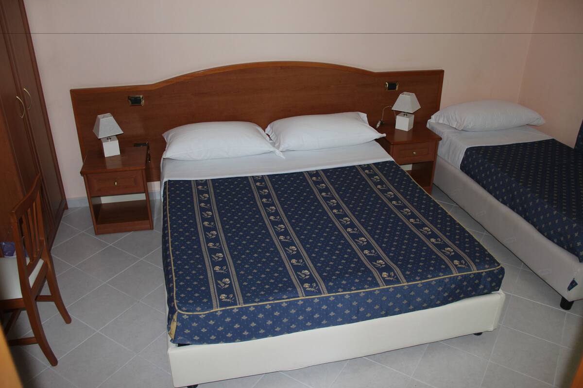 Una cama doble con colcha azul estampada, dos mesitas de noche con lámparas y un cabecero de madera.