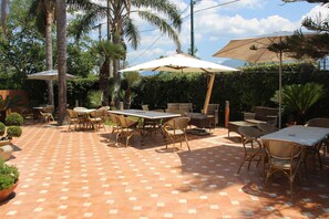 Um pátio externo com piso de azulejos, várias mesas e cadeiras, e guarda-sóis.
