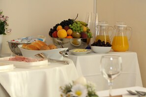Mesa de café da manhã com uma fruteira, jarras de suco e diversos itens para o café.