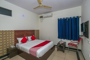 A hotel room with a bed, a desk, a chair, a ceiling fan, an air conditioning unit, a TV, and a patterned wall. - GKS Residency (Bengaluru)