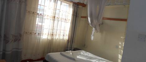 A room with a bed, a chair, and a window with curtains.