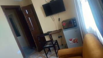 Una sala de estar con un sofá, un televisor montado en la pared, un microondas y una puerta que da a otra habitación.