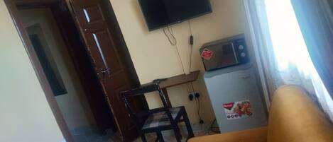 A living room with a sofa, a television mounted on the wall, a microwave, and a door leading to another room.