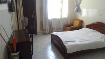 Un dormitorio con cama, una silla, un escritorio y un ventilador.
