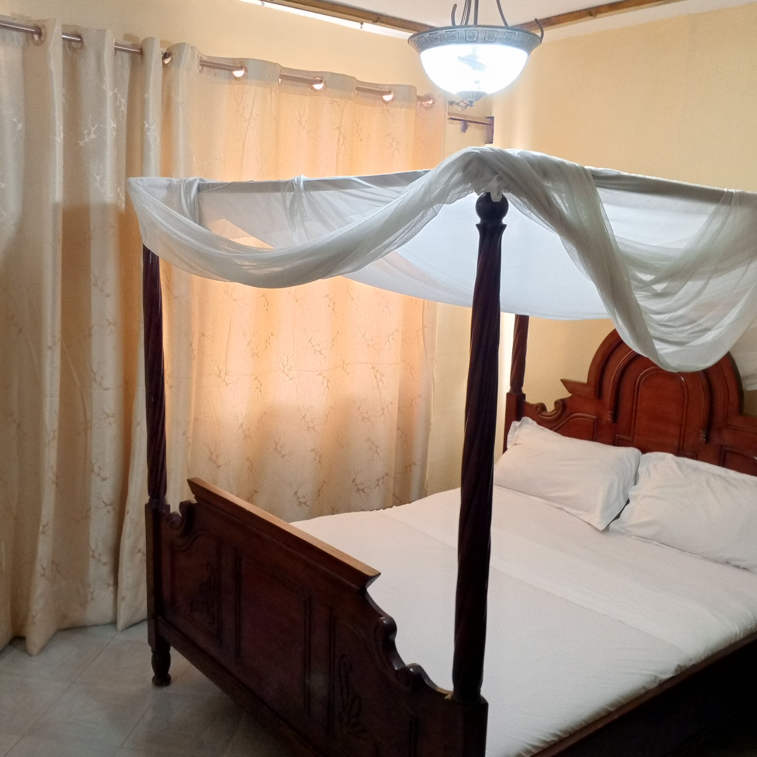 A four-poster bed with a canopy, wooden headboard, and white bedding.