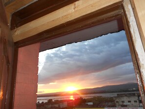 A sunset view through a window with a brick wall and a wooden beam structure.