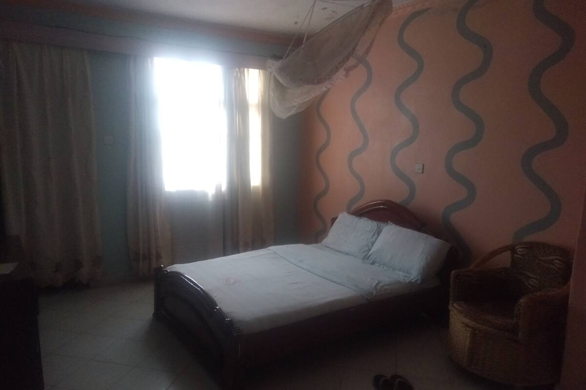 Een slaapkamer met een bed, een stoel en een paar schoenen op de vloer.