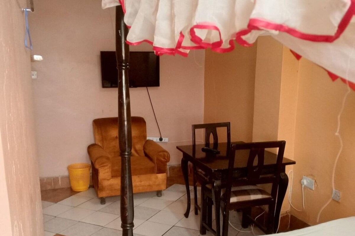 Une pièce comprenant un lit, une chaise en bois, une table et un téléviseur fixé au mur.