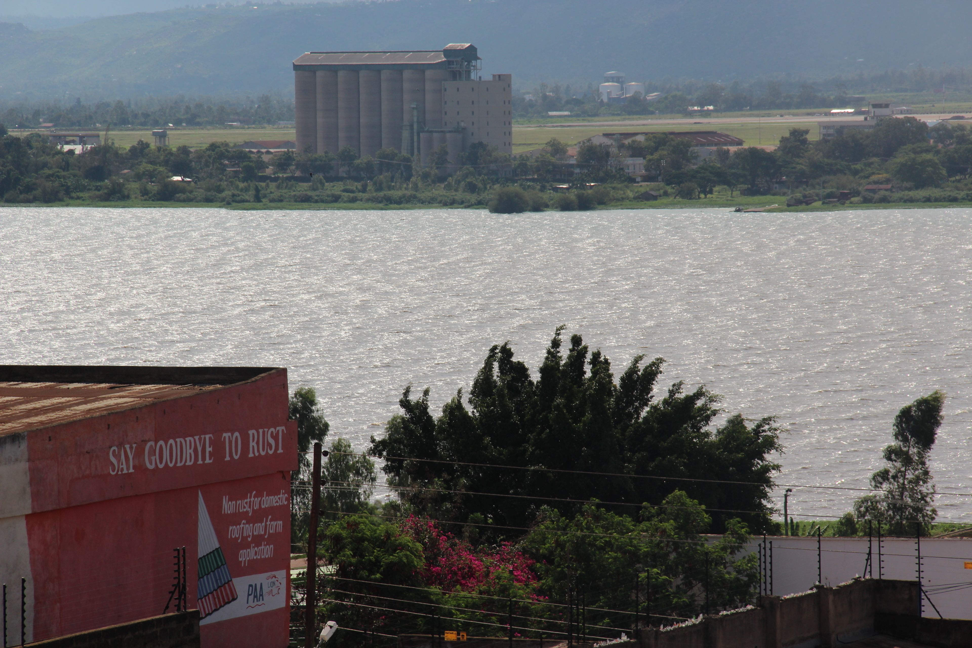 A view of a river with a large industrial building in the background and a sign with text.