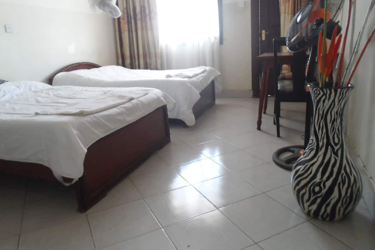 Een hotelkamer met twee bedden, een stoel, een ventilator en een vaas.