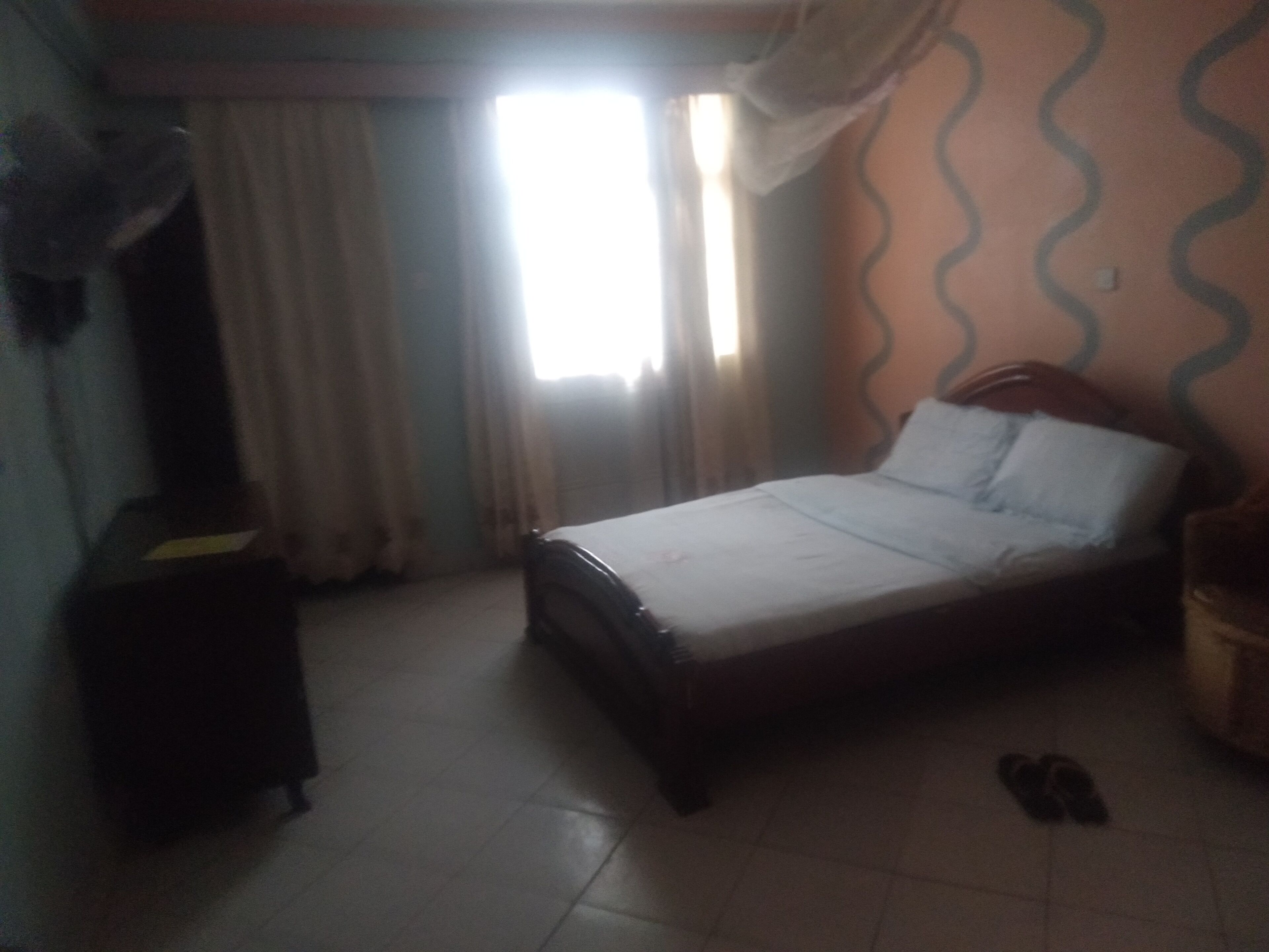 A bedroom with a bed, a nightstand, a lamp, a window with curtains, and a patterned wall.