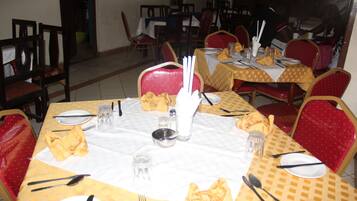 Un espace repas avec des tables disposées pour accueillir plusieurs personnes, des chaises et une variété d’articles de vaisselle.
