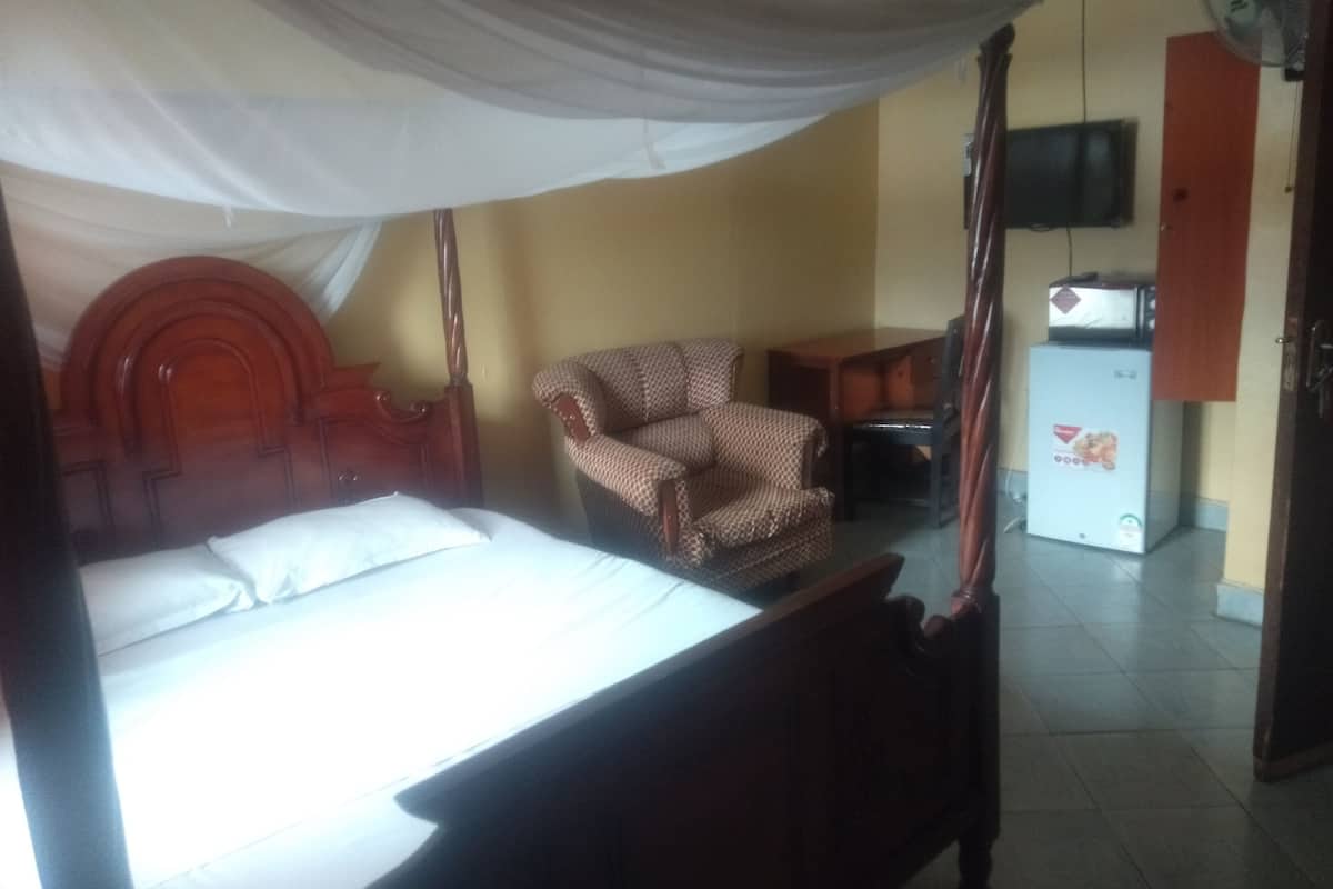 Een slaapkamer met een bed, een stoel, een televisie en een koelkast.