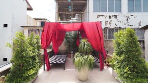 A courtyard with a checkered bench, red drapes, and potted plants. - Zent & Bao Hostel (Bangkok)