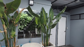 A bathroom with a large sink, two potted plants, a decorative stone basin, and a tiled floor. - Zent & Bao Hostel (Bangkok)