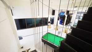 A modern interior with a pool table, a staircase, and a view of the outside. - Zent & Bao Hostel (Bangkok)