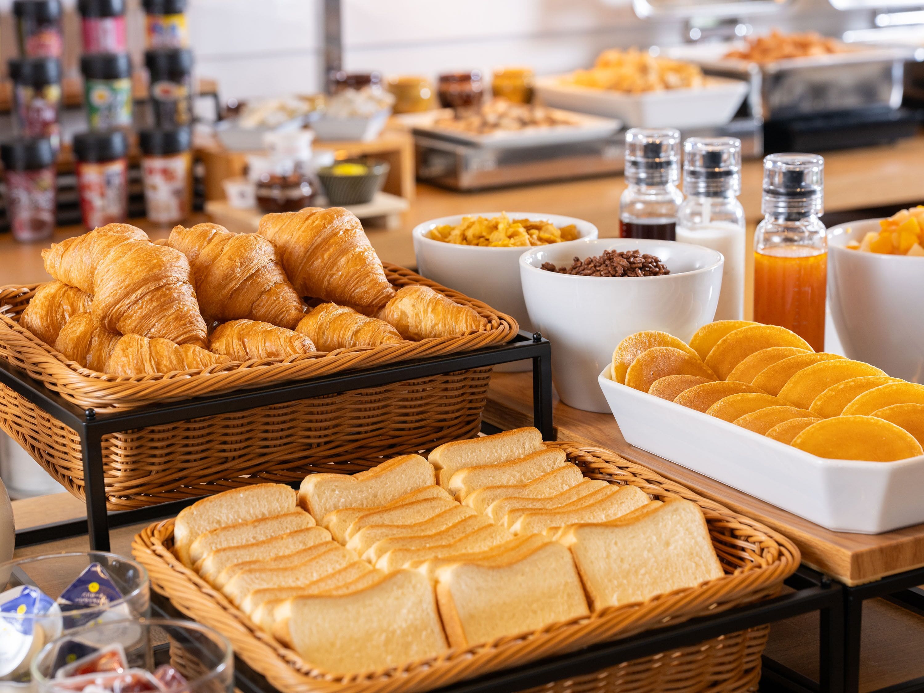 A breakfast buffet with bread, pastries, and condiments.