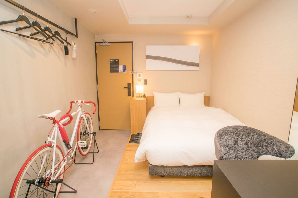 A hotel room with a bed, a bicycle, a coat rack, and a door with a sign.