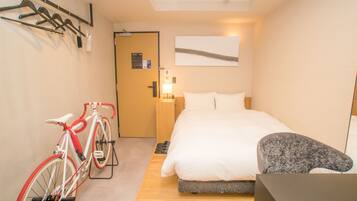 A hotel room with a bed, a bicycle, a coat rack, and a door with a sign.