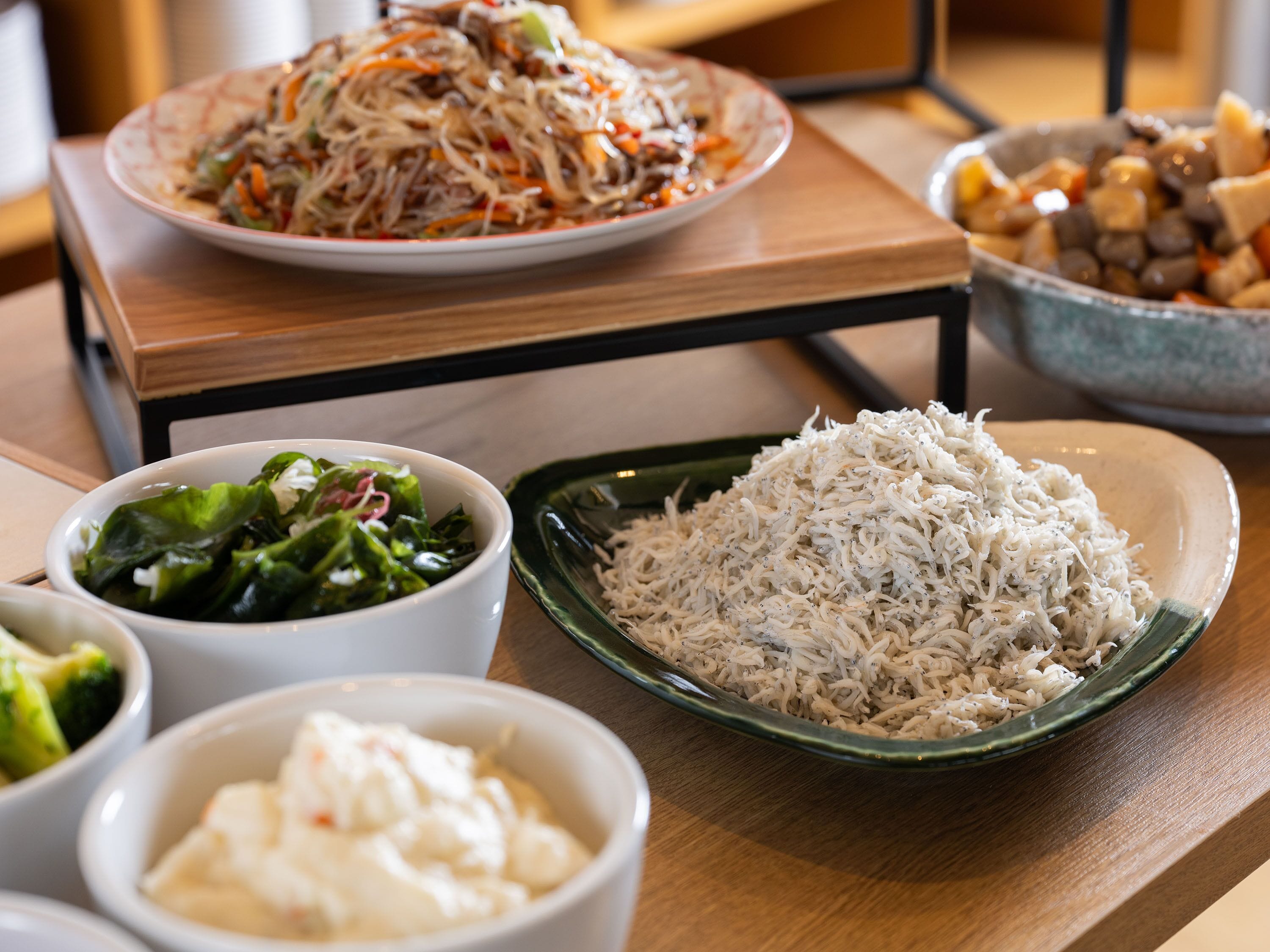 A dining table with various dishes including rice, vegetables, and a noodle dish.