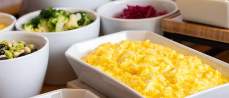 Buffet com diversos pratos, incluindo macarrão com queijo, legumes e salsichas.