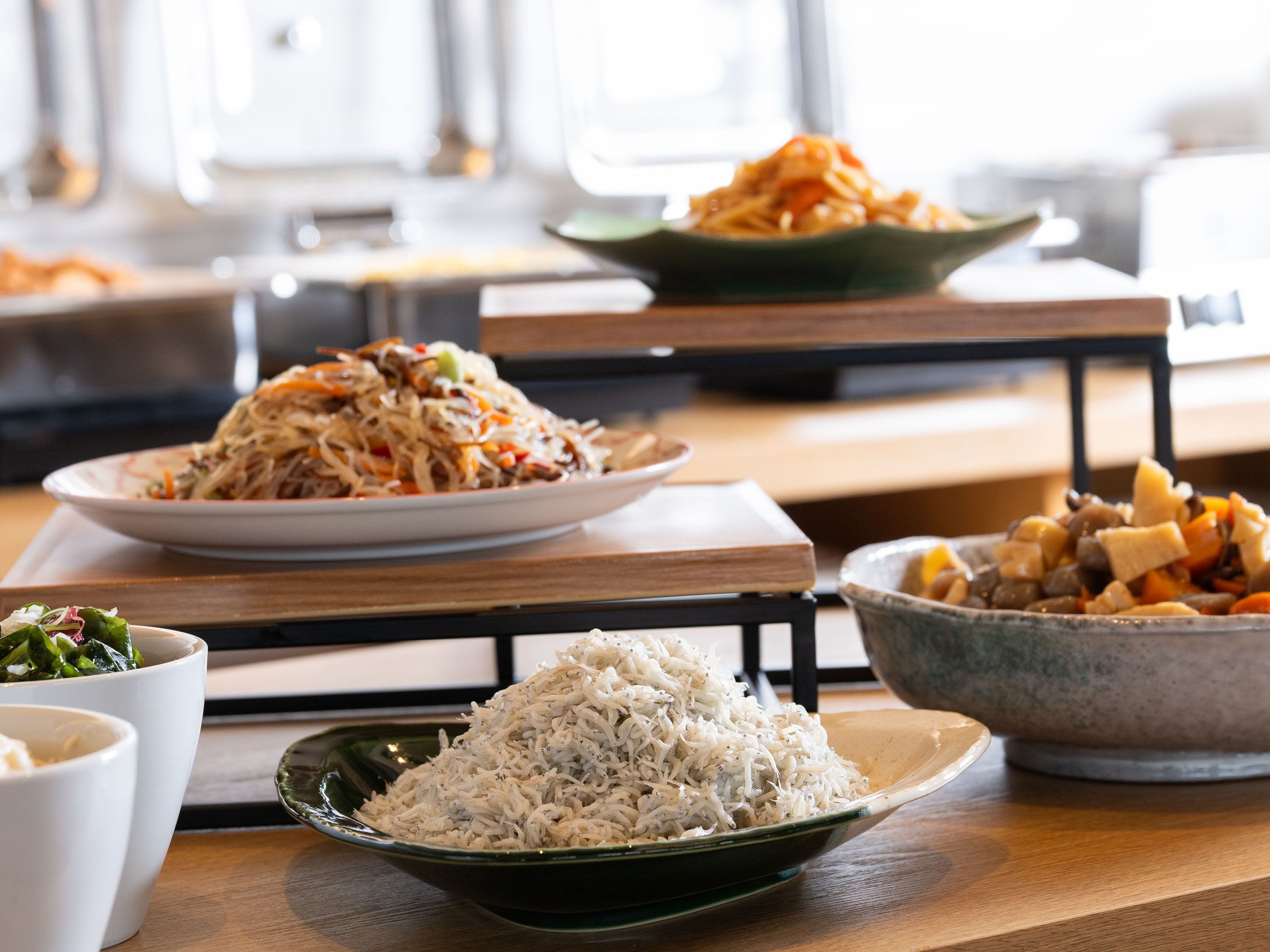 Una mesa de comedor con diversos platos, incluyendo un tazón de arroz, un plato de fideos y un tazón de verduras mixtas.