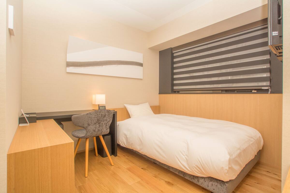 A compact hotel room with a bed, a desk, and a chair.