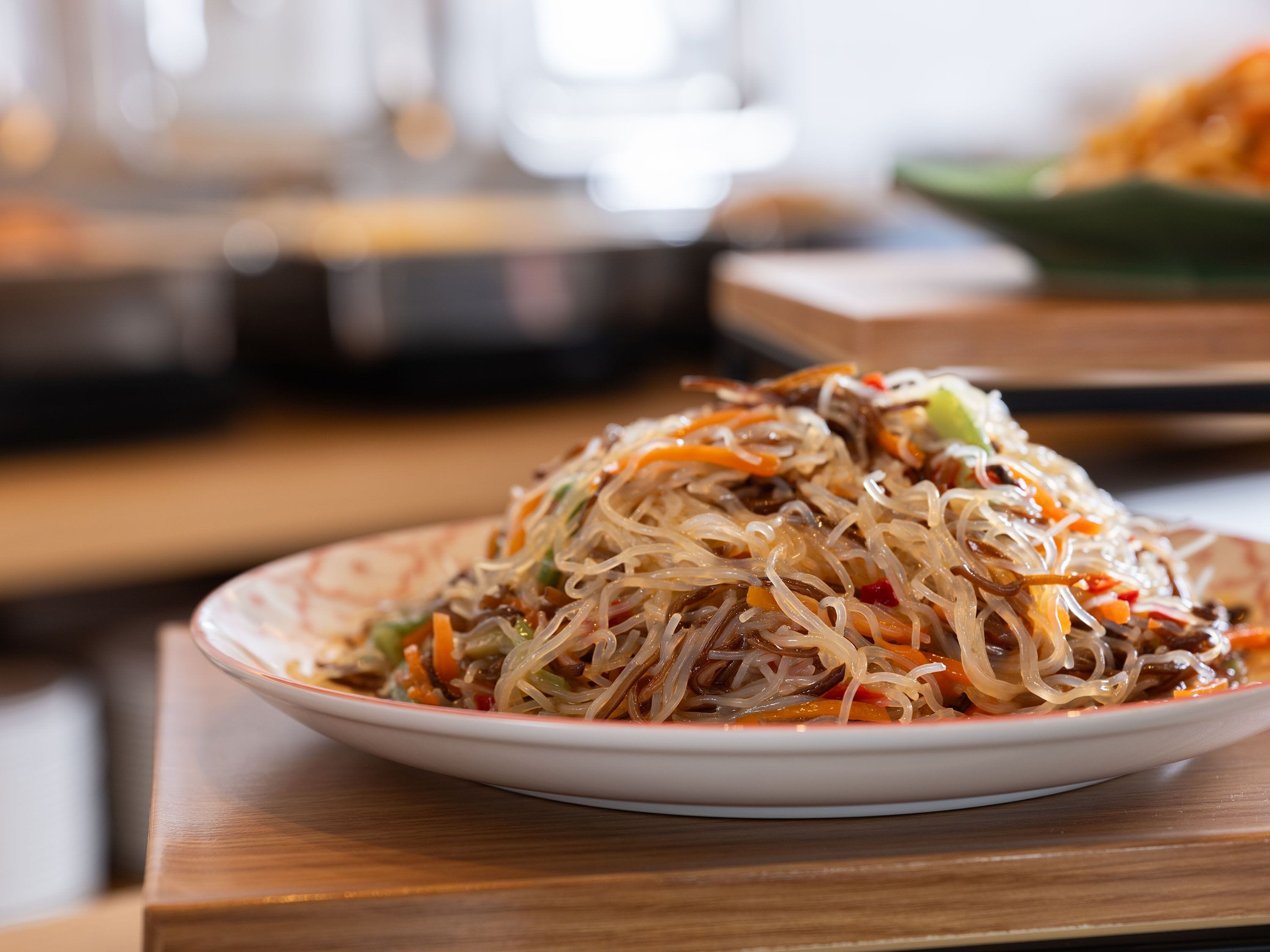 A plate of noodles with vegetables and meat, placed on a table.