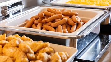 A buffet with various food items including sausages, macaroni, and fried chicken.