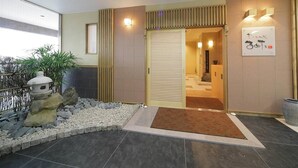 A hotel entrance with a tiled floor, a stone lantern, a small rock garden, and a wooden door. - Hagi Royal Intelligent Hotel (Hagi)