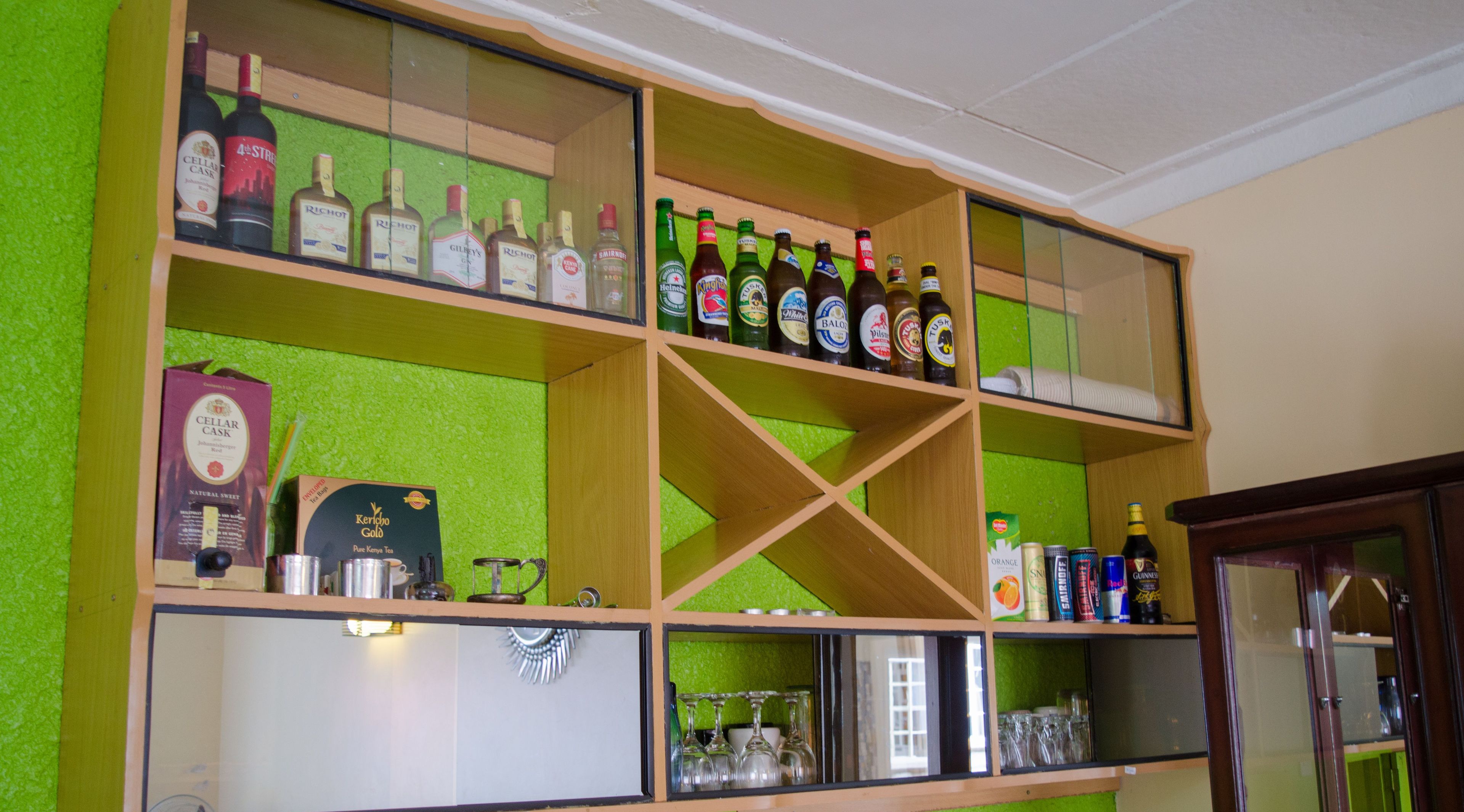 Zona de bar con estantes llenos de diferentes botellas de licor, una máquina de café y vasos.