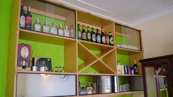 Zona de bar con estantes llenos de diferentes botellas de licor, una máquina de café y vasos.