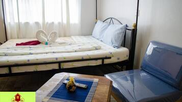 A bedroom with a bed, a blue chair, a small table with a remote control, and a decorative towel on the bed.