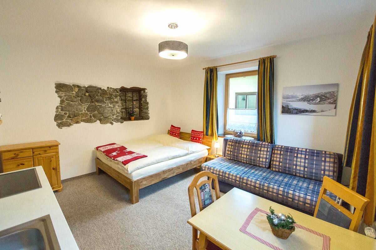 A cozy room with a bed, a sofa, a table, and a stone wall.