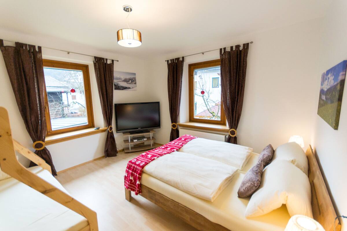 A bedroom with a bed, a TV, and two windows with curtains.
