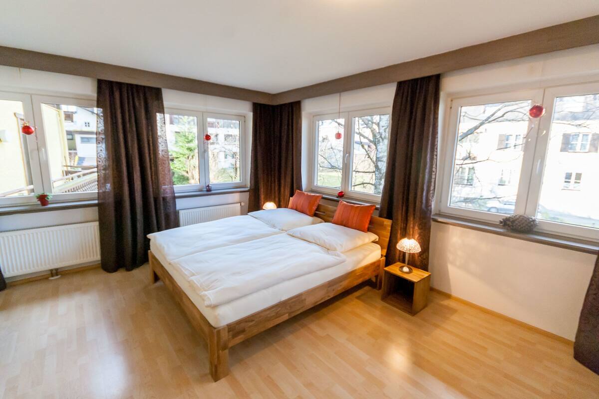 A bedroom with a wooden bed, two bedside tables, and large windows with curtains.