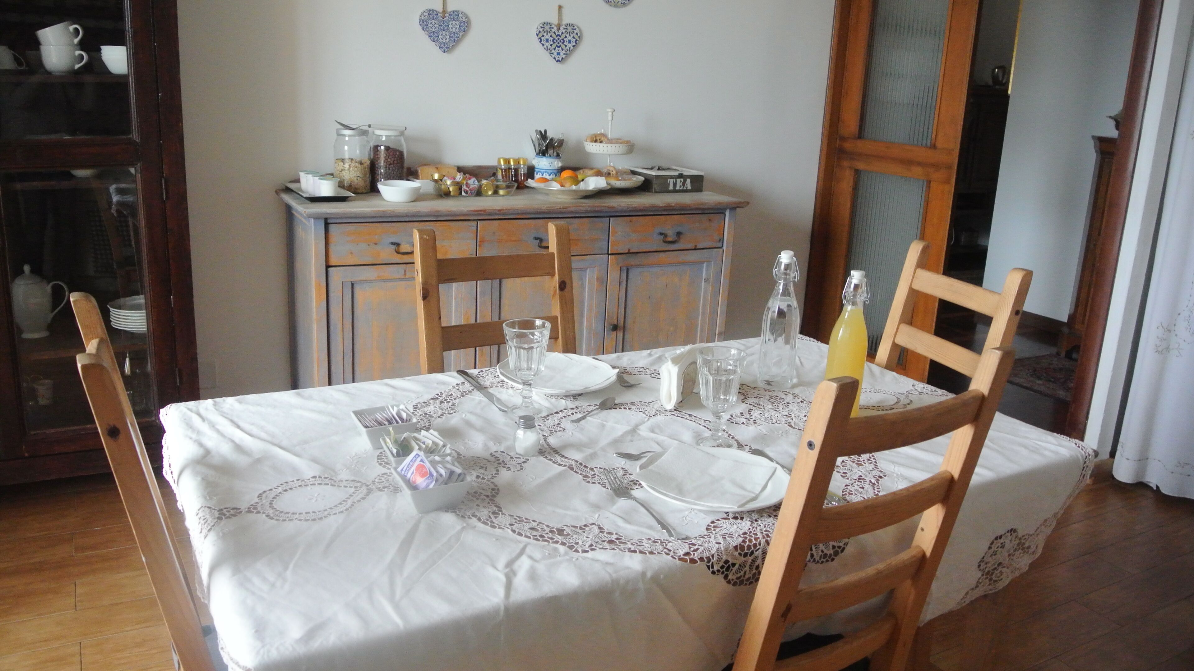 Une table à manger recouverte d’une nappe blanche agrémentée de détails en dentelle, entourée de chaises en bois.