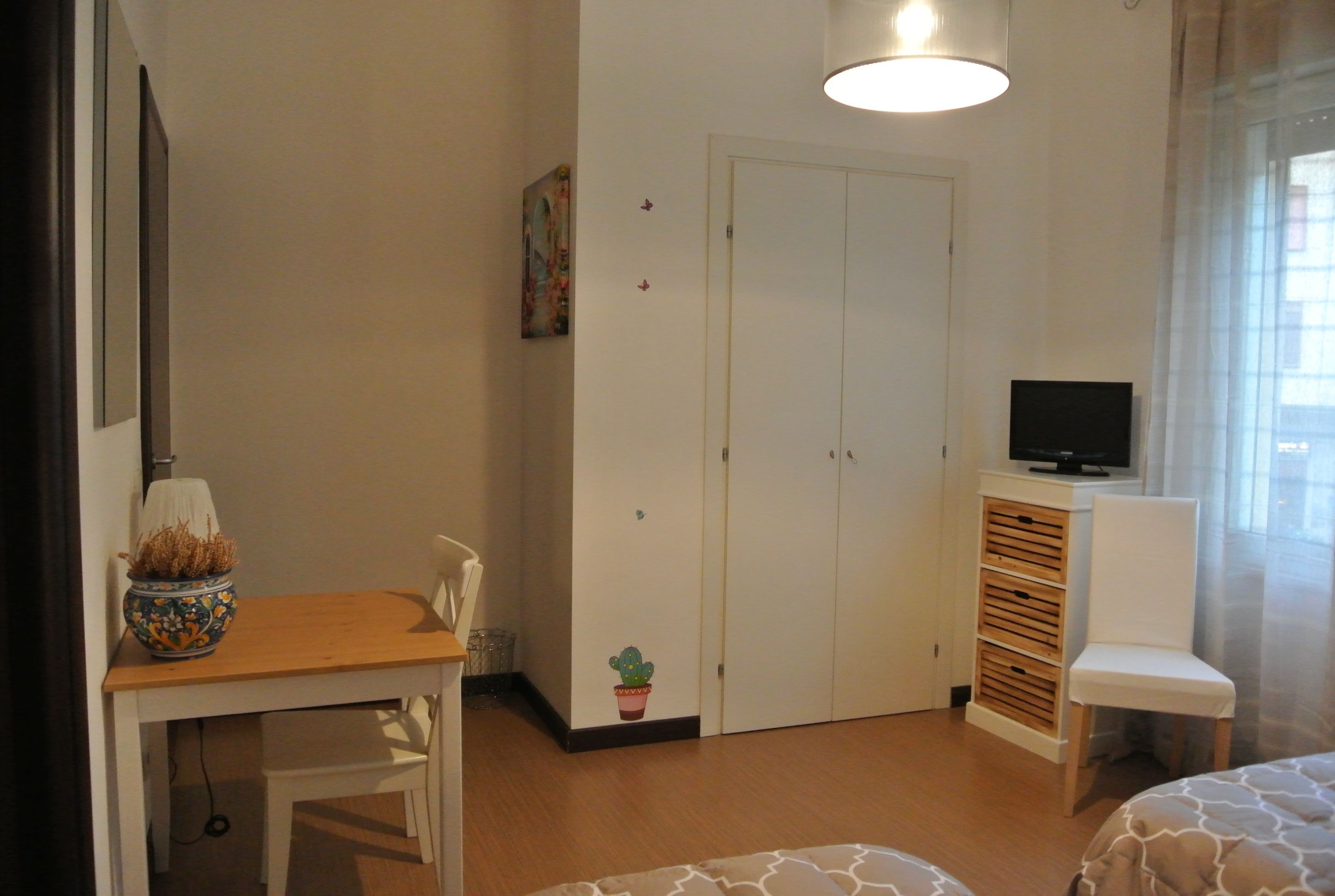 A bedroom with a wooden table, a TV on a cabinet, a wardrobe, and a bed.