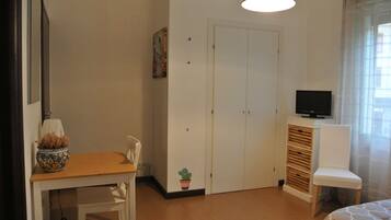 A bedroom with a wooden table, a TV on a cabinet, a wardrobe, and a bed.