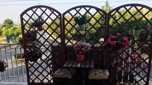 A patio area with a wooden table and two cushioned chairs, surrounded by a lattice fence with hanging planters. - B&B Via dei Templi (Agrigento)