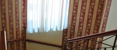 A staircase with a handrail, patterned wallpaper, and a window with sheer curtains.