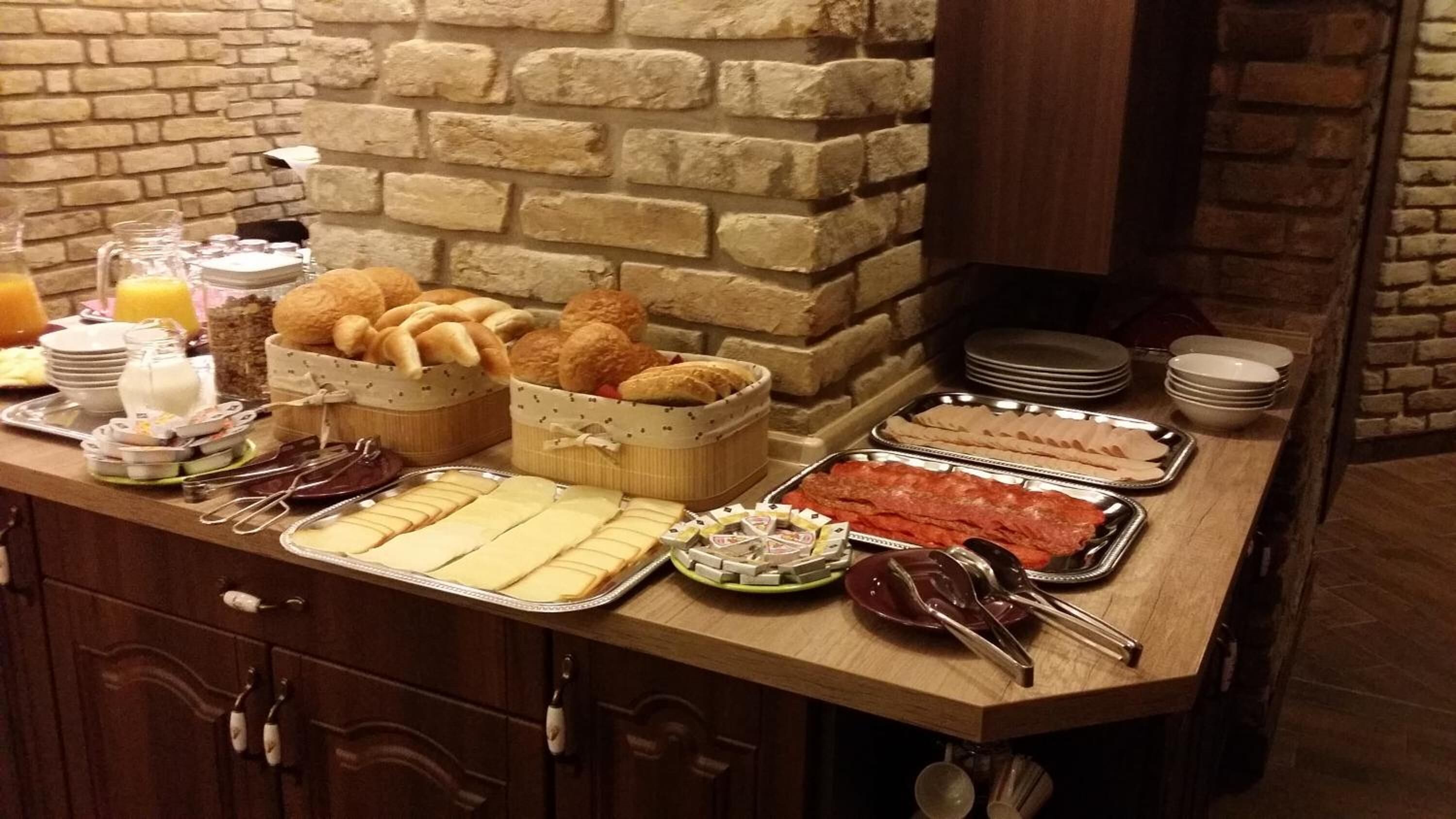 A buffet with various food items, including bread, cheese, and meats, arranged on a wooden counter with a stone wall backdrop.