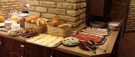 A buffet with various food items, including bread, cheese, and meats, arranged on a wooden counter with a stone wall backdrop.