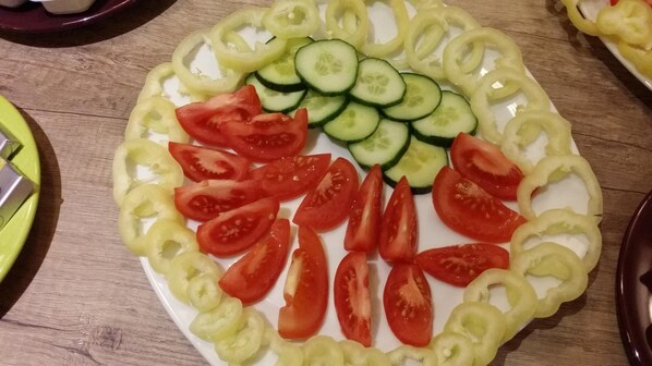 Un plato con rodajas de verduras, entre ellas tomates, pepinos y pimientos, sobre una mesa de madera.