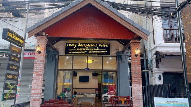 A hostel with a red roof and tiled entrance. There are signs for 'Lucky Backpackers Hostel' and 'Flight Ticket'. - Lucky Backpacker Hostel (Vientiane)