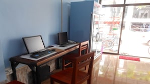 A workspace with two desks, each with a computer and keyboard. There are two chairs, one at each desk. The room has a blue wall and a glass door leading outside. - Lucky Backpacker Hostel (Vientiane)