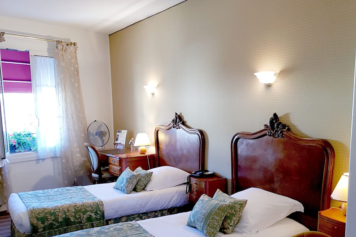 A hotel room with two beds, a chair, a desk, and a window with curtains.