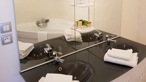 A bathroom with a large mirror, a black sink, a bathtub, and a shelf with toiletries. - Hostellerie du Grand Sully (Sully-sur-Loire)